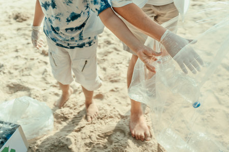 A father and son are working together to collect trash at the beach and place it in recycling bags. Family help clean up seaside that are dirty.の写真素材