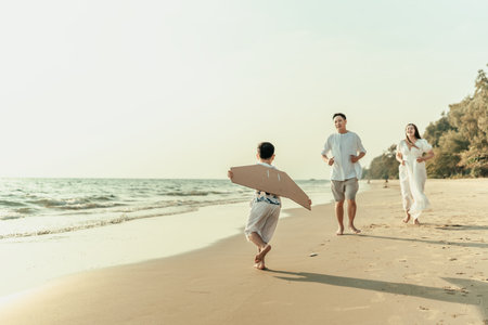 Wearing paper airplane wings makes a boy feel like they are traveling and running on the beach happiness with family together while on a holiday, travel, long weekend, summer, or any other holiday.の写真素材