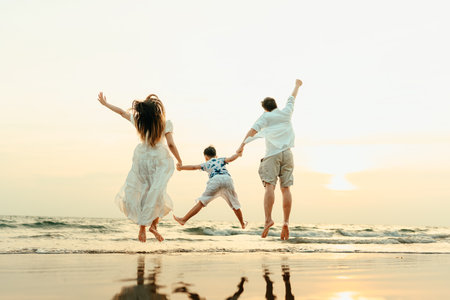Family jumping happily with their hands raised, having fun on the beach with family during a holiday, travel, long weekend, summer or any other holiday. They are happy to spend time together.の写真素材