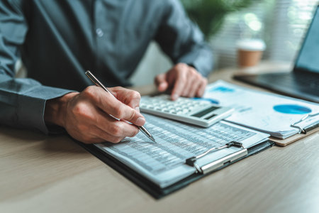 A close-up view of a businessman hand gripping a pen, indicating a project along with financial report on paper document, symbolizing data analysis, corporate, team and business strategy planning.の写真素材