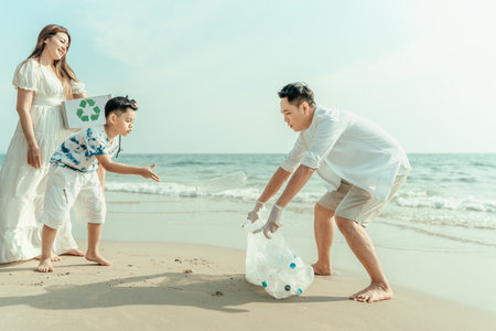 The son of an Asian family is throwing plastic bottles picked up from the beach in a garbage bag that his father is carrying for recycling or reuse. Dirty beachの写真素材