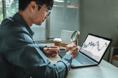 Businessman is hand holding magnifying glass and point to laptop screen represent to search . Business report graph and chart, corporate, finance and marketing concept.の写真素材