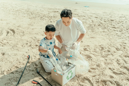 A father and son are removing trash from the beach and putting it in boxes for recycling. Family make sure dirty seaside are cleaned up.の写真素材