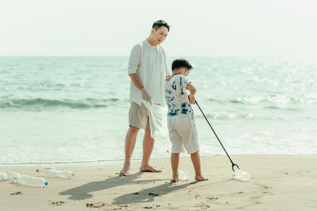On the beach, a father and son carry bags to collect trash. Clean up the dirty sea or ocean and collect reusable plastic bottles. Garbage recycling.の写真素材