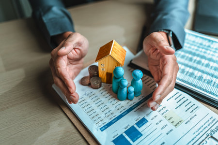 Businessman's hand gestures to protect money, house, wooden dolls represent family. Image represents the concept of asset protection, emphasizing safeguarding financial investments and propertyの写真素材