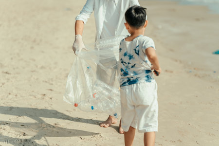 On the beach, a father and son carry bags to collect trash. Clean up the dirty sea or ocean and collect reusable plastic bottles. Garbage recycling.の写真素材