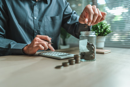 Businessman putting coins saving money with jar coin on desk. income, deposit, financial planning and investment concept.の写真素材