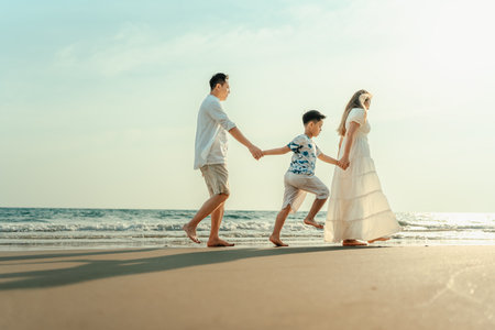 On vacation, travel, or a long weekend, spend time together with family and have fun and happiness by walking hand in hand on a beautiful beach with sunset light.の写真素材