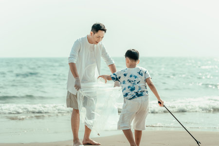 On the beach, a father and son carry bags to collect trash. Clean up the dirty sea or ocean and collect reusable plastic bottles. Garbage recycling.の写真素材
