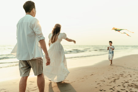 Mom and Dad watch their kids happily fly kites on the beach during a holiday, travel, long weekend, summer or any other holiday. They are happy to spend time together.の写真素材