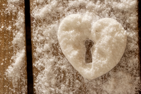Snow heart with a keyhole on a wooden surface.の写真素材