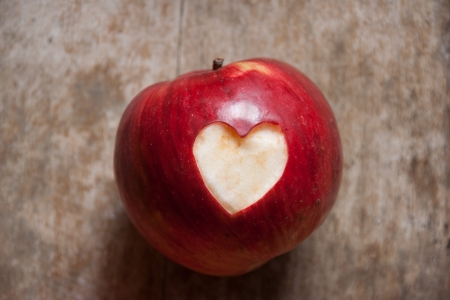 Ripe red apple with a heart shape neatly cut of the skin on a textured weathered wooden surfaceの写真素材