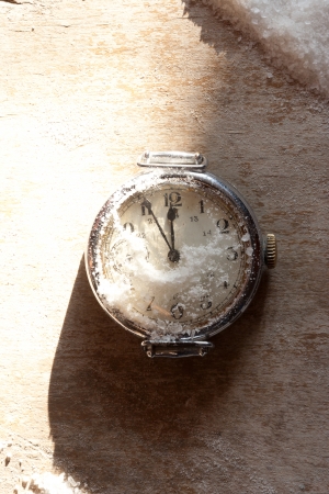 Watch lying in the snow before the new year, wooden surfaceの写真素材