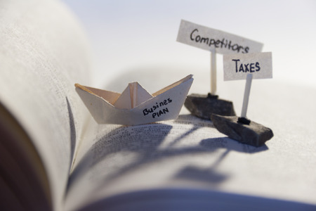 Business concept. Open book and a paper boat with word Business Plan and tags competitors, taxes.の写真素材