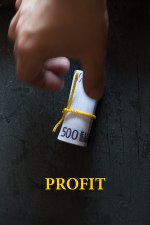 Profit - Business Concept. Roll of money on a dark table hand and an inscription.の写真素材