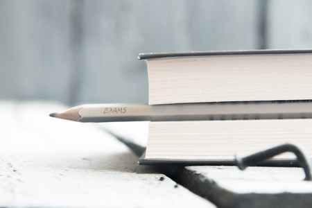 Exams idea. ? pencil and a book on the table, exams inscription in pencil. Toned photo.の写真素材