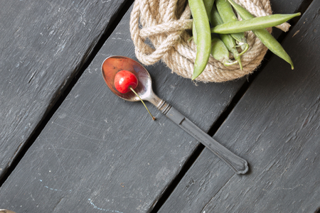 spoon with a cherry on an old black table and green beansの写真素材