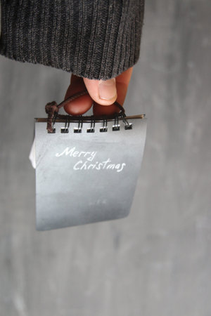 Merry Christmas card, hand holds a tag with the inscription