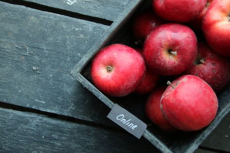 Grocery online shop idea. Ripe red apples in wooden box and tag with the inscription online. Soft focus.の写真素材