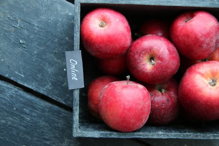 Grocery online shop idea. Ripe red apples in wooden box and tag with the inscription online.の写真素材