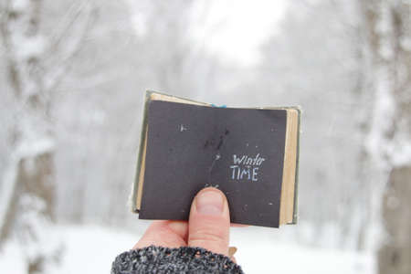 Winter time concept. A hand holds a book with the inscription on the background of the winter forest.の写真素材