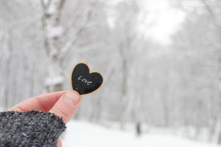 Valentine's day concept. Hand holds a heart on the background of a snowy forest.の写真素材
