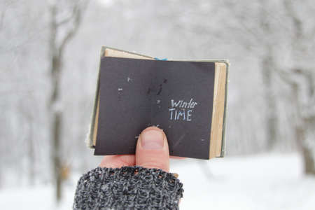 Winter time concept. A hand holds a book with the inscription on the background of the winter forest.の写真素材