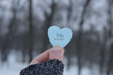 A hand holds a paper blue heart with the inscription Hello winterの写真素材