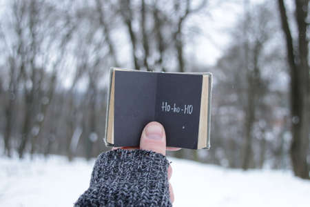 A hand holds a book with an inscription on the background of a winter park. Ho-ho-hoの写真素材