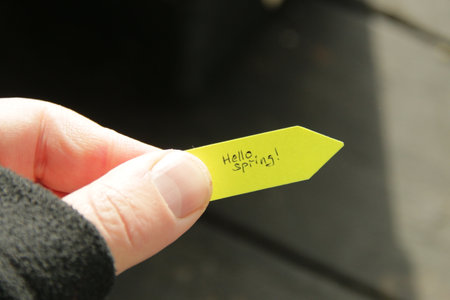 Hello spring. The hand holds a tag with a handwritten inscription.の写真素材