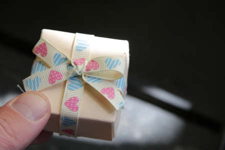 A mans hand holds a gift box with a ribbon.の写真素材