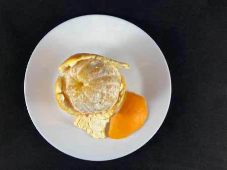On a white plate - a half-peeled orange. A plate with an orange on a black surface.の写真素材
