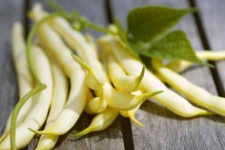 Yellow beans with leaves lying on a wooden tableの写真素材