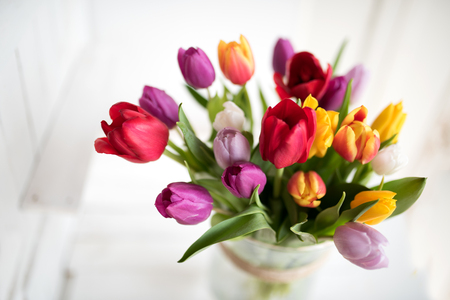 Spring bouquet with colorful tulips on a white wooden table for mothers day or birthday greetingsの写真素材