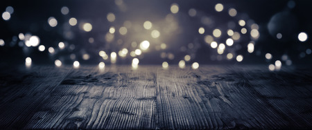 Gold and silver bokeh on a dark background with empty wooden floor for a festive conceptの写真素材