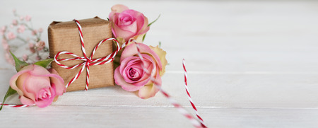 Tender pink roses with a gift on white wooden background and bokeh for mothers dayの写真素材