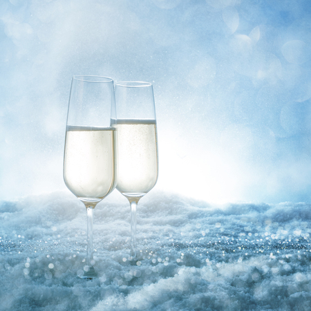Two champagne glasses in frosty snow with blue bokeh skyの写真素材