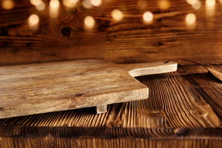 Empty wooden cutting board on rustic wooden table with golden bokeh for a decorationの写真素材