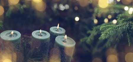 Green advent candles with fir tree outdoors and golden bokeh for a christmas background