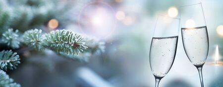 Frozen fir branches in winter and champagne glasses in the foreground. Short depth of field and solid golden bokeh with space for text.の写真素材
