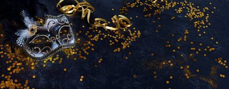 mask with golden confetti and streamers on dark blue background. Background decoration for traditional mardi gras with space for text and design.の写真素材