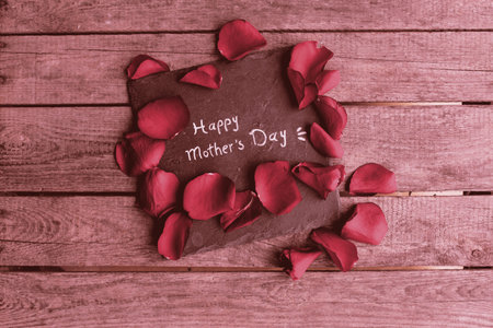 Red roses petals with a slate for mother's day on old wooden planks. Top view with space for text.