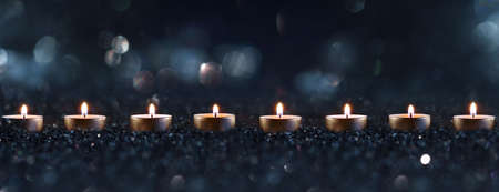 Candlelights in the darkness with blurred golden bokeh. Horizontal background with short depth of field for religious rituals and spiritual meditation or grief.の写真素材