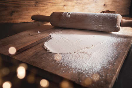 Baking utensils and flour for christmas cookies on wooden cutting board with golden bokeh. Background for christmas baking. Short depth of field with space for decorations and text.の写真素材