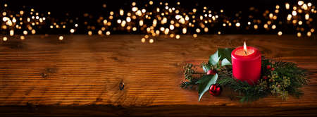 Background for christmas with burning red candle and natural decoration on rustic wooden board. Background with festive golden bokeh lights and space for your text.の写真素材