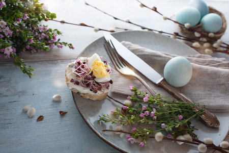 Floral easter place setting for a breakfast with cream cheese and radish seeds on gray vintage wood....