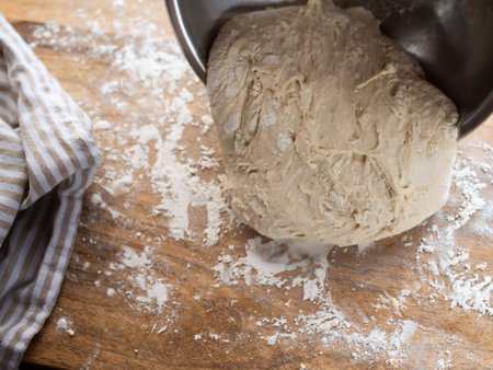 Dough processing with flour for a homemade baguette on a wooden kitchen counter.