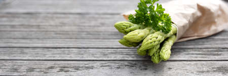 Healthy green asparagus and parsley on gray wooden planks. Fresh ingredients for a seasonal gastronomy concept. Horizontal background with short depth of field and space for text.の写真素材