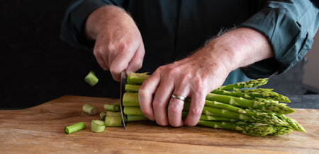 Hands cutting green asparagus on a wooden cutting board. Vegetables for a healthy eating concept....