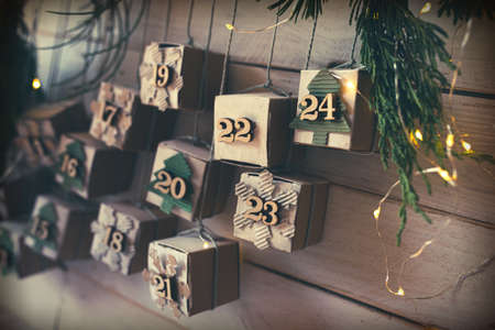 Homemade small carton boxes for advent surbrises with fairy light. Hanging vintage advent calendar made of cardboard for a environmentally conscious christmas. Close-up with short depth of field.の写真素材